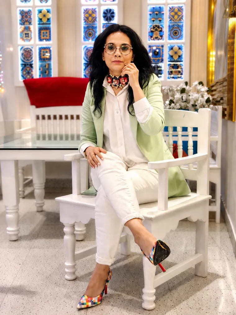 Maliha Bano seated on a white carved chair wearing colourful patchwork heels